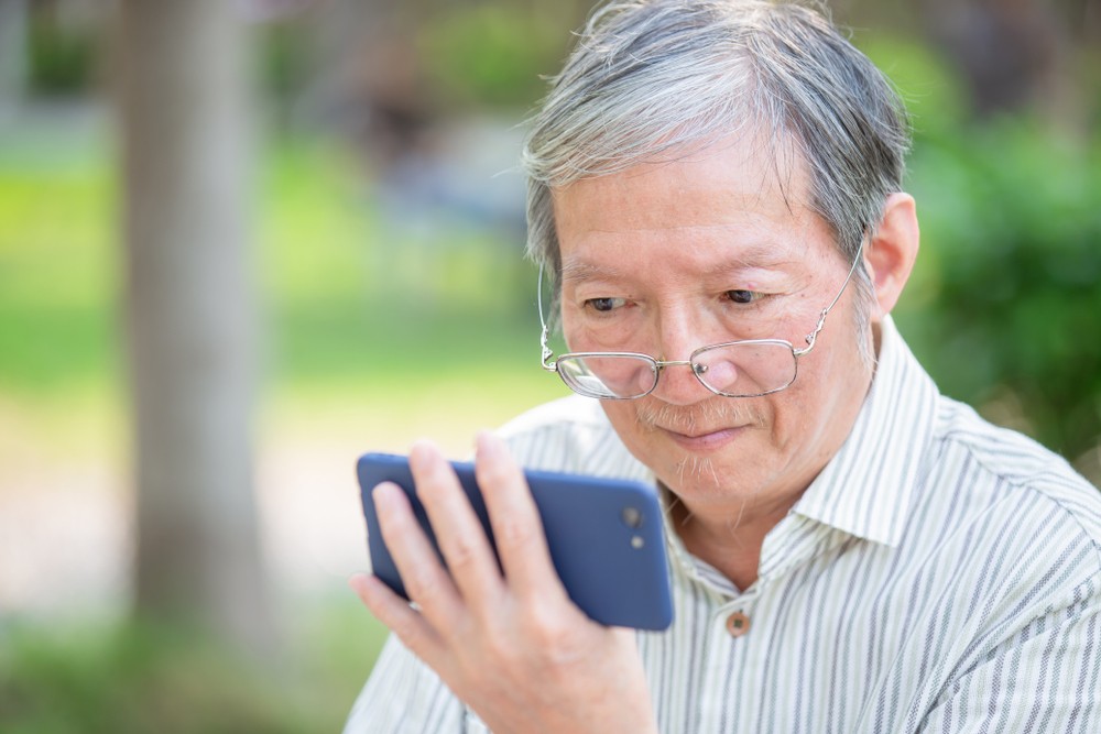 Older man take off the glasses and watch video by cellphone in the park