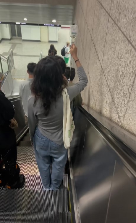 發現扶手梯有位女子右肩背著手袋,手上還拿著一個剩下半瓶藥劑的吊瓶。